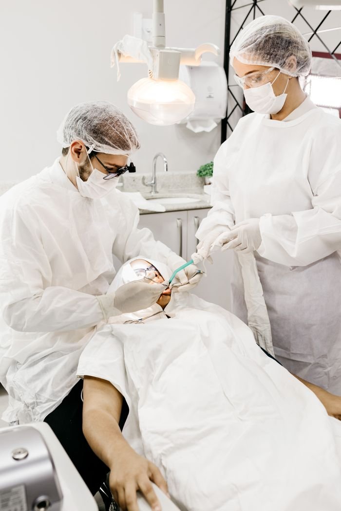Home From above of anonymous orthodontist and assistant in white uniforms treating teeth of man using medical instruments in clinic